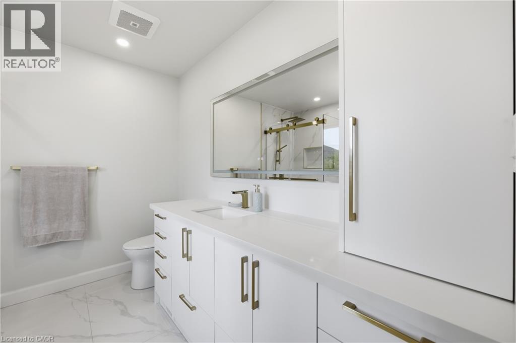 Recessed lighting with a built-in exhaust fan, white vanity with gold hardware, integrated rectangular sink, large frameless mirror, and white tile flooring - 738 Fourth Line, Milton, ON - Indoor Photo Showing Bathroom