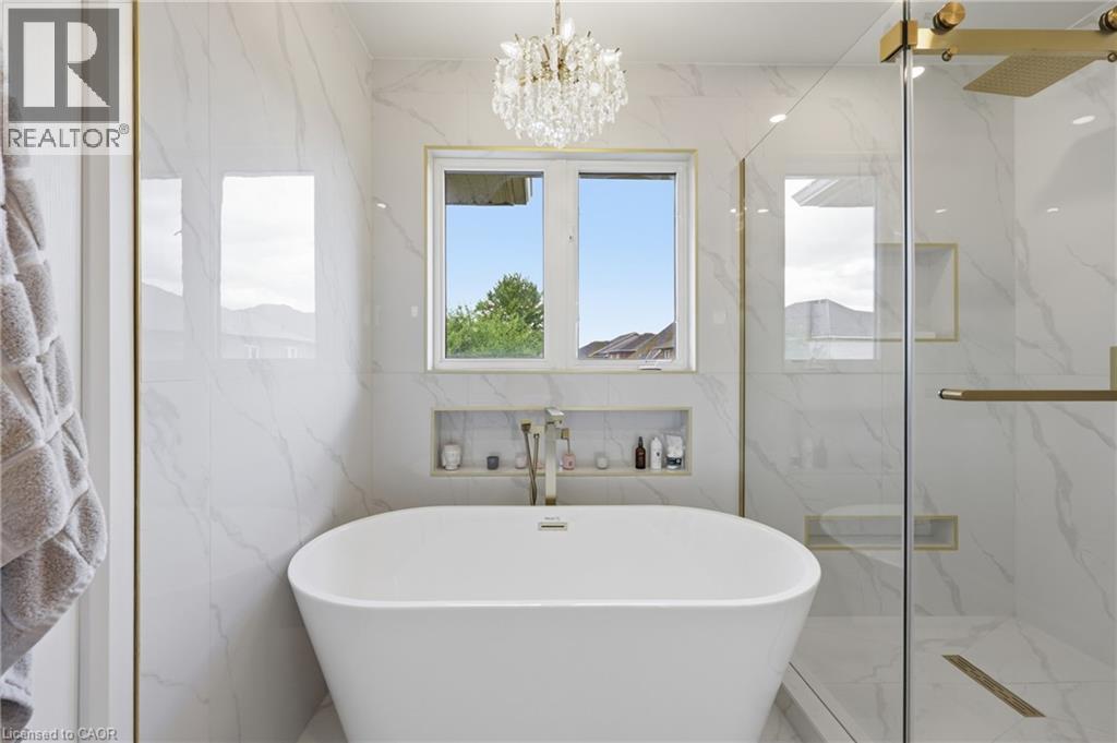 Freestanding soaking tub with a wall-mounted faucet, complemented by a walk-in shower featuring a glass enclosure and built-in shelving - 738 Fourth Line, Milton, ON - Indoor Photo Showing Bathroom