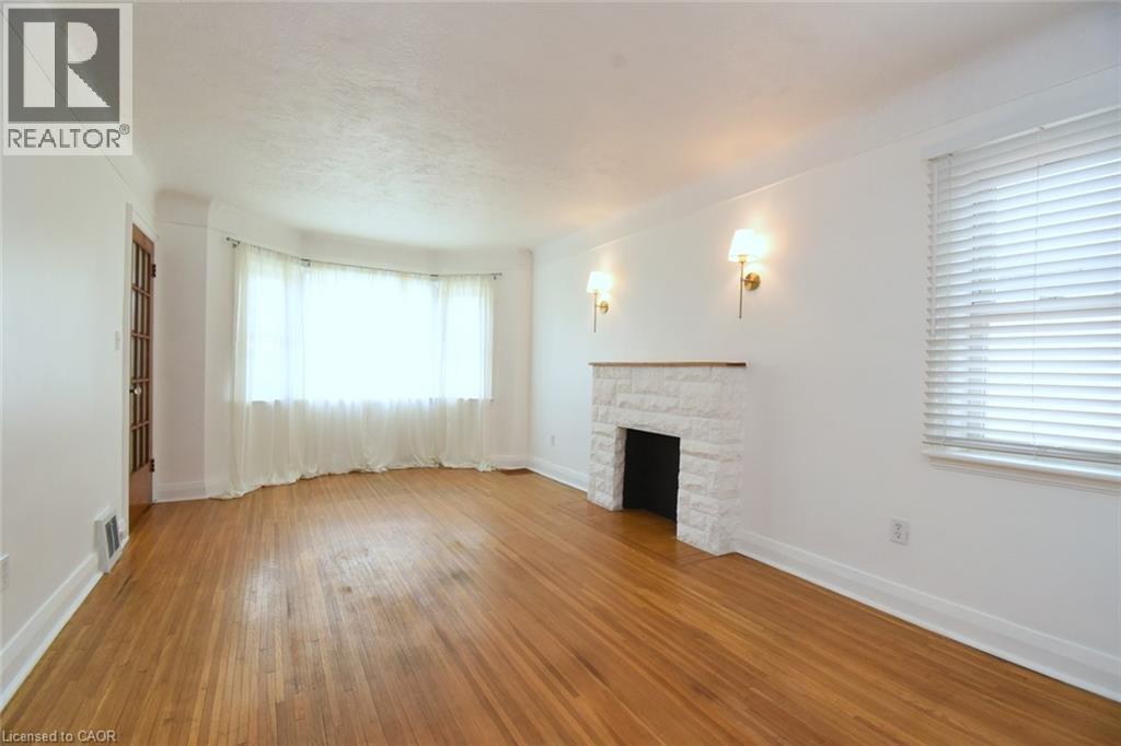 Hardwood flooring throughout, a white stone fireplace with wood mantel, multiple wall sconces, a bay window with sheers, and a dark wood-finish interior door - 575 Upper Wentworth Street, Hamilton, ON - Indoor With Fireplace