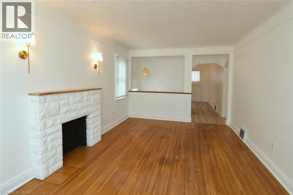 Wood-finish flooring, white stone-clad fireplace with wood mantle, wall-mounted sconce lighting, and window with blinds - 575 Upper Wentworth Street, Hamilton, ON - Indoor Photo Showing Other Room With Fireplace