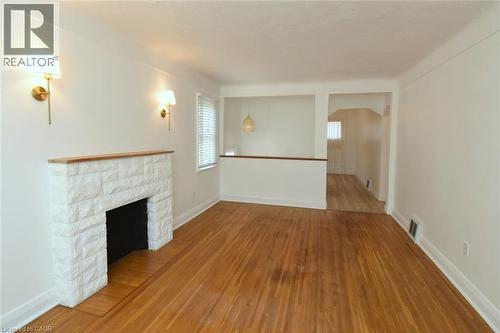Wood-finish flooring, white stone-clad fireplace with wood mantle, wall-mounted sconce lighting, and window with blinds - 575 Upper Wentworth Street, Hamilton, ON - Indoor Photo Showing Other Room With Fireplace