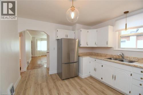 White cabinetry with decorative hardware, stainless steel refrigerator, double basin sink, wood-finish flooring, and a contemporary pendant light fixture - 575 Upper Wentworth Street, Hamilton, ON - Indoor Photo Showing Kitchen With Double Sink