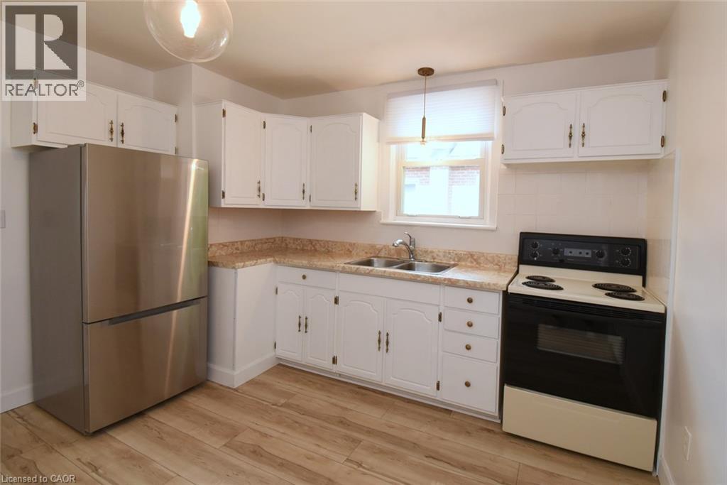 Kitchen featuring wood-finish flooring, white cabinetry, a stainless steel refrigerator, and a double-basin sink - 575 Upper Wentworth Street, Hamilton, ON - Indoor Photo Showing Kitchen With Double Sink