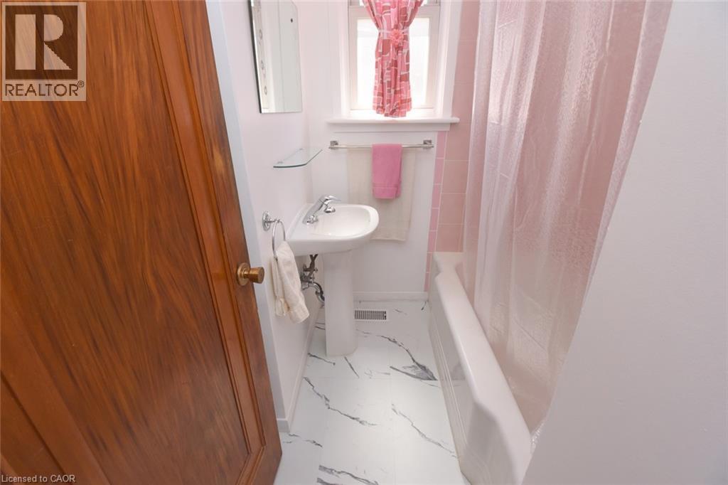 Pedestal sink with chrome fixtures, white bathtub, pink tiled shower surround, and a window for natural light - 575 Upper Wentworth Street, Hamilton, ON - Indoor Photo Showing Bathroom