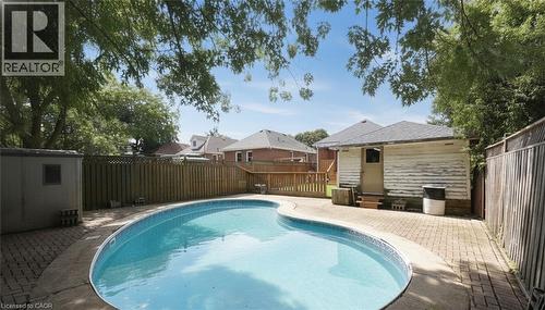 Curved swimming pool with a surrounding paver patio, wood privacy fencing, and mature trees - 575 Upper Wentworth Street, Hamilton, ON - Outdoor With In Ground Pool With Backyard