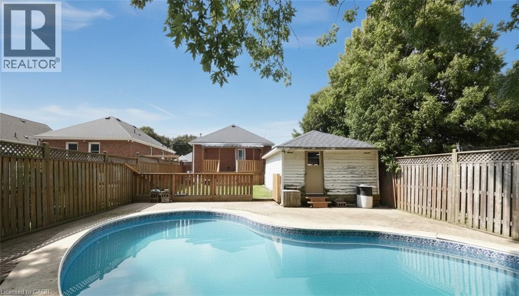 Rear yard featuring an in-ground swimming pool, surrounding paver patio, wood fencing, and a detached outbuilding - 575 Upper Wentworth Street, Hamilton, ON - Outdoor With In Ground Pool With Backyard