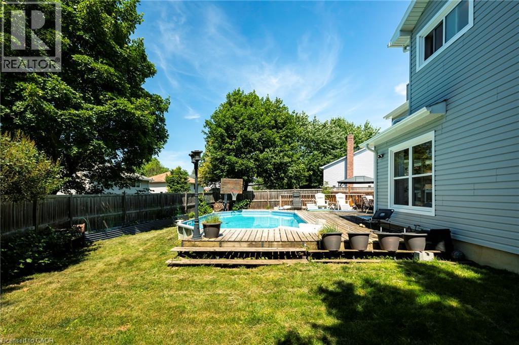 Expansive backyard featuring a manicured lawn, a swimming pool with a surrounding wood deck, and a privacy fence - 364 Stoneheight Place, Waterloo, ON