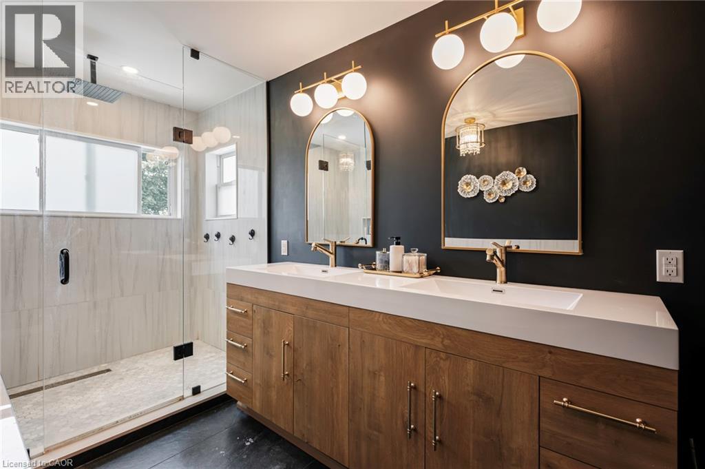 Dual-sink vanity with wood-finish cabinetry, gold-tone fixtures, and arched mirrors - 364 Stoneheight Place, Waterloo, ON