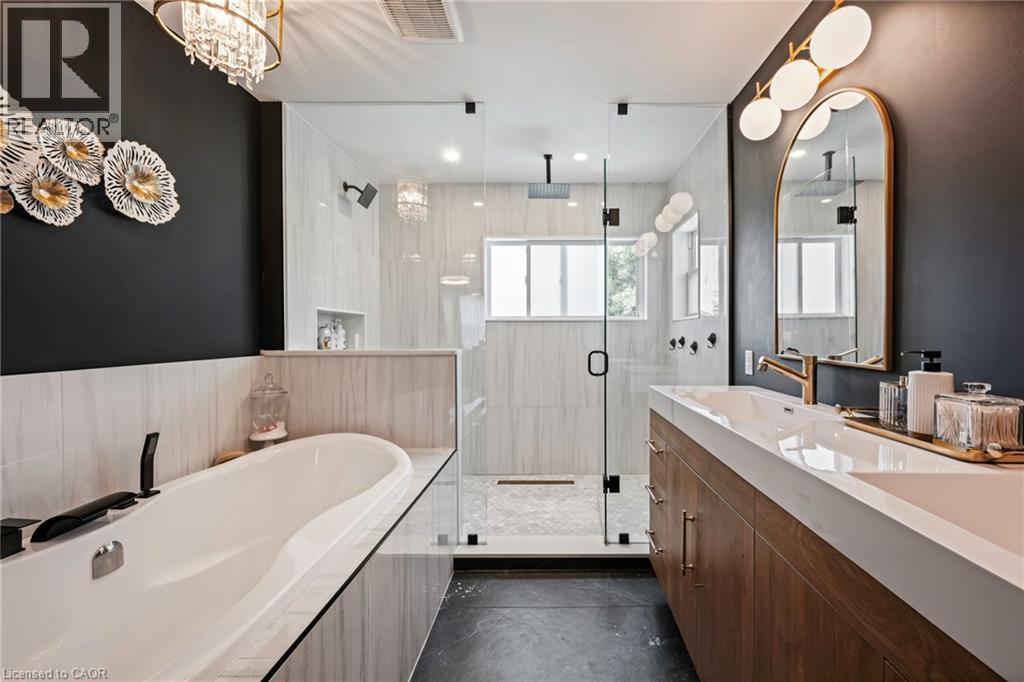 Freestanding soaking tub, glass-enclosed shower, wood-finish double vanity, white countertop with integrated sinks, and gold-tone fixtures - 364 Stoneheight Place, Waterloo, ON