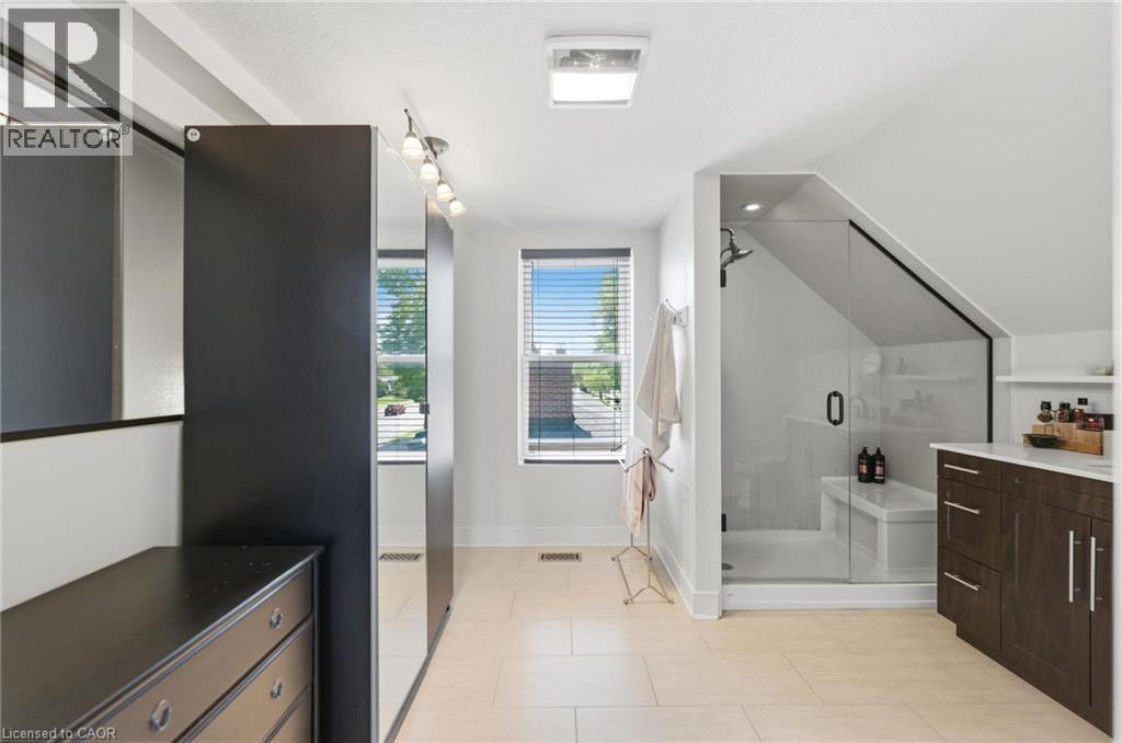 Light-toned tile flooring complements a spacious bathroom featuring a glass-enclosed shower with a built-in bench - 69 Nash Road S, Hamilton, ON