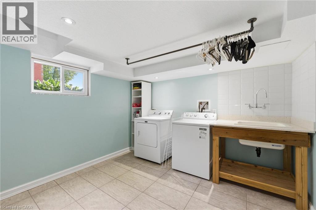 Laundry area featuring recessed lighting, a utility sink with a stone-finish countertop, a wooden base cabinet, and tile flooring - 69 Nash Road S, Hamilton, ON