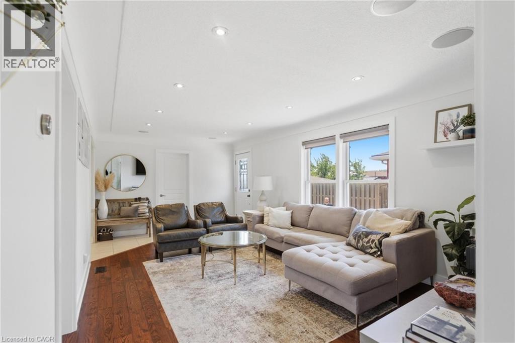 Bright living area featuring wood-finish flooring, recessed lighting, and large windows with white trim - 69 Nash Road S, Hamilton, ON