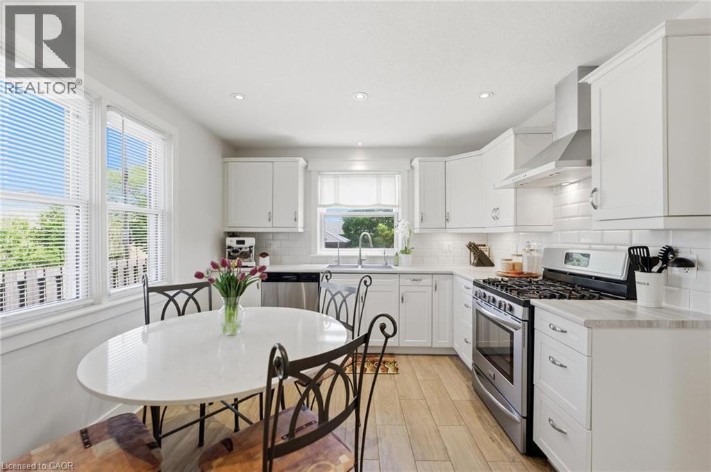Contemporary kitchen featuring white cabinetry, stainless steel appliances, a subway tile backsplash, and light wood-finish flooring - 69 Nash Road S, Hamilton, ON