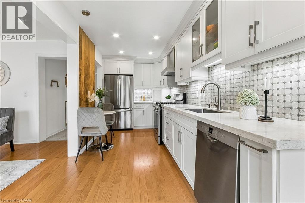 Kitchen featuring light wood-finish flooring, white cabinetry, integrated stainless steel appliances, a tile backsplash, and light-toned countertops - 1373 Quest Circle, Mississauga, ON
