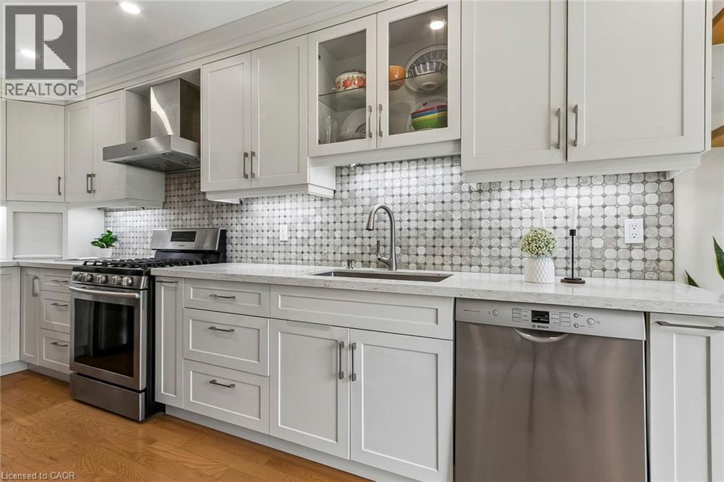 White shaker-style cabinetry, stainless steel appliances, patterned tile backsplash, light-toned countertops, and wood-finish flooring - 1373 Quest Circle, Mississauga, ON