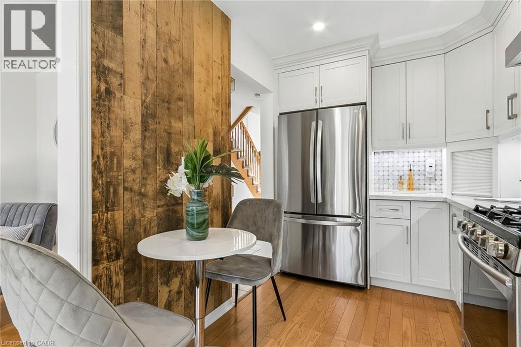 Kitchen featuring white cabinetry, light wood-finish flooring, stainless steel refrigerator, white backsplash, and gas range - 1373 Quest Circle, Mississauga, ON
