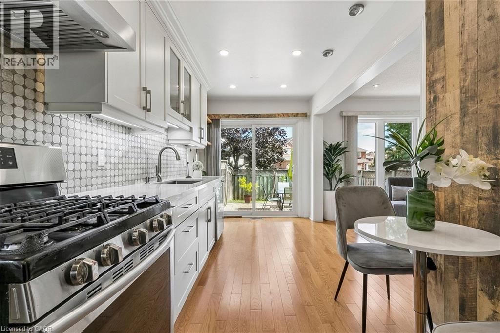 Contemporary kitchen featuring light wood-finish flooring, white cabinetry, integrated stainless-steel appliances, a mosaic tile backsplash, and recessed lighting - 1373 Quest Circle, Mississauga, ON