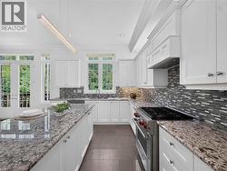 White cabinetry, granite countertops, tile backsplash, stainless steel range, and French doors -