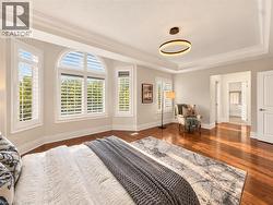 Hardwood flooring, tray ceiling, crown molding, modern circular pendant lighting, and arched window with plantation shutters -