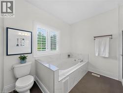 Jetted soaking tub with marble-look tile surround, white plantation shutters, and dark flooring -