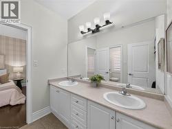 Dual undermount sinks set in a light-toned countertop, white cabinetry with silver-toned hardware, and a large wall-mounted mirror with a four-light fixture -