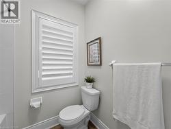 White plantation shutters framing a window, white toilet, tile wall, and a towel bar -