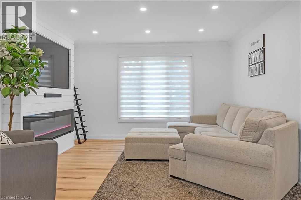 Recessed lighting, wood-finish flooring, white shiplap fireplace surround, built-in linear fireplace, and window with layered shades - 4236 Longmoor Drive, Burlington, ON