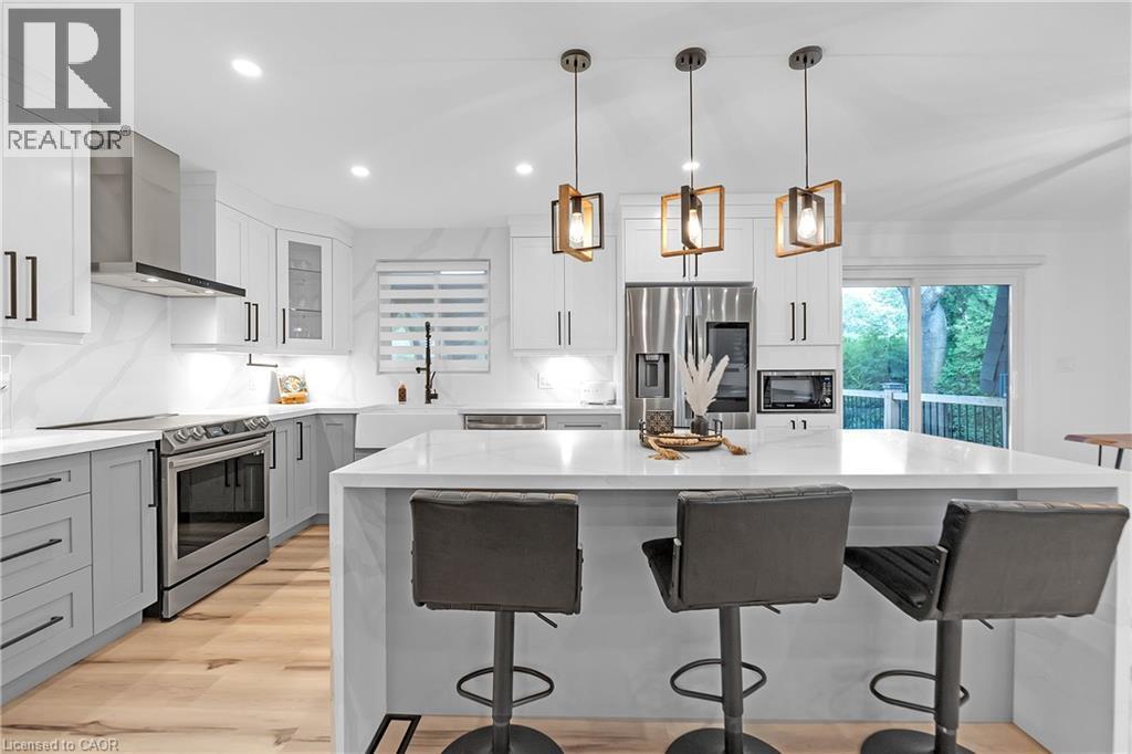 Kitchen featuring wood-finish flooring, white and gray cabinetry, built-in stainless steel appliances, a large center island, and contemporary pendant lighting - 4236 Longmoor Drive, Burlington, ON