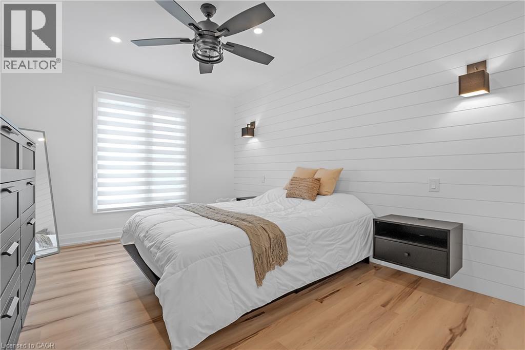 Wood-finish flooring, white shiplap accent wall, modern ceiling fan, and built-in wall sconces - 4236 Longmoor Drive, Burlington, ON