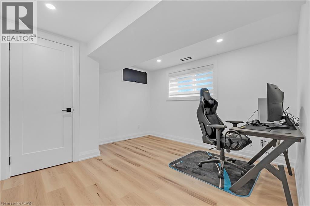 Recessed lighting, wood-finish flooring, white trim, modern interior door with matte black hardware, and an egress window - 4236 Longmoor Drive, Burlington, ON