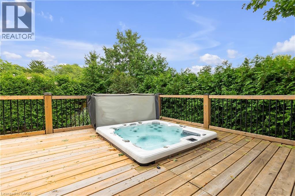 Wood deck with an integrated spa, featuring wood railing posts and black metal balusters, surrounded by mature privacy hedges - 4236 Longmoor Drive, Burlington, ON