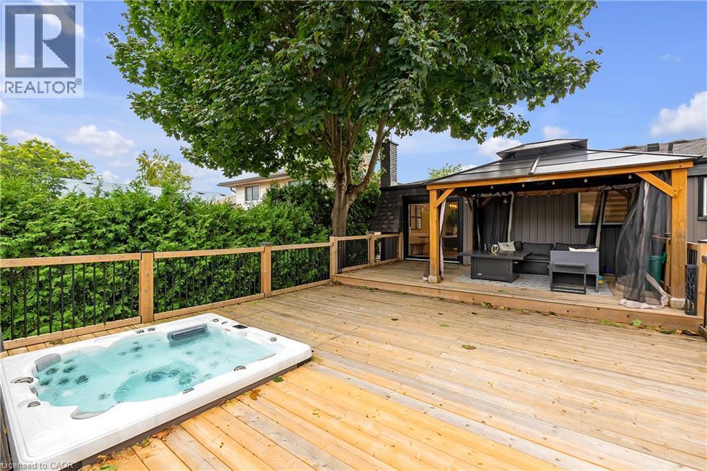 Expansive wood deck with a built-in spa, wood and metal railing, and a covered patio area - 4236 Longmoor Drive, Burlington, ON
