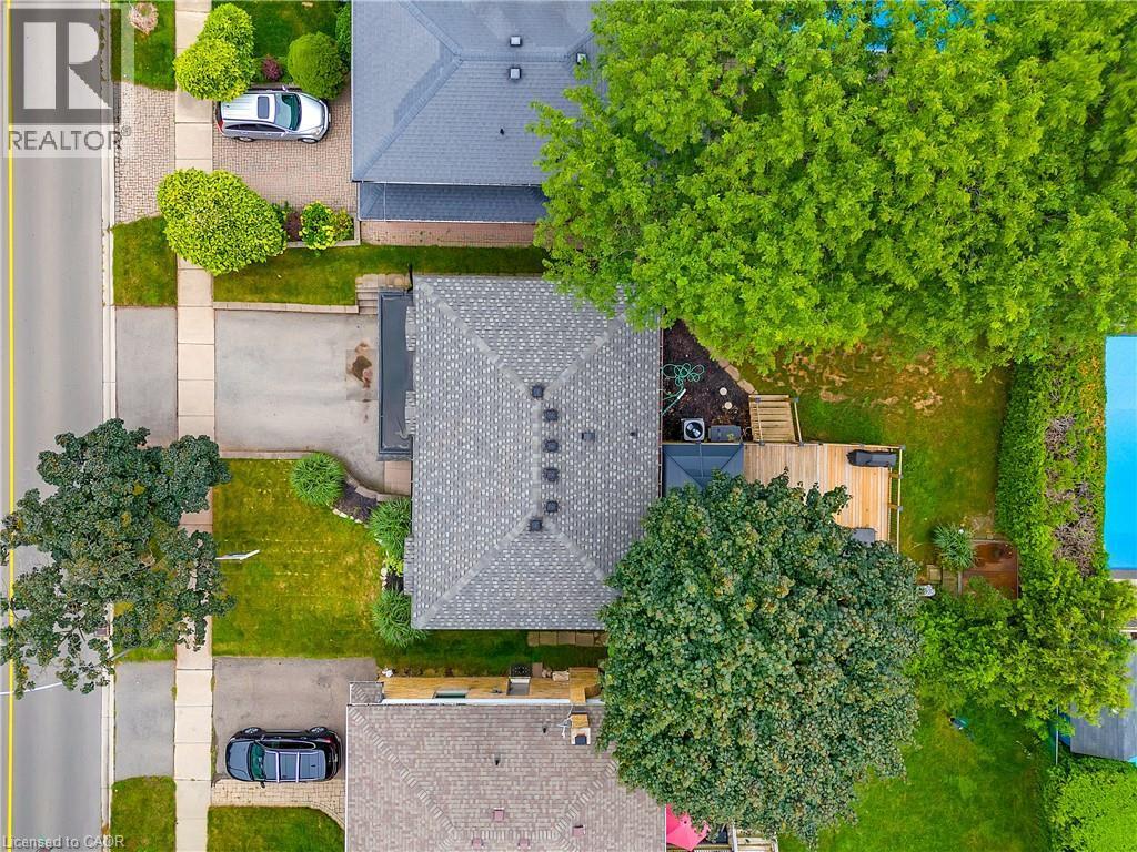 Shingled roof, paved driveway, expansive grassy areas, wooden deck, and mature trees - 4236 Longmoor Drive, Burlington, ON