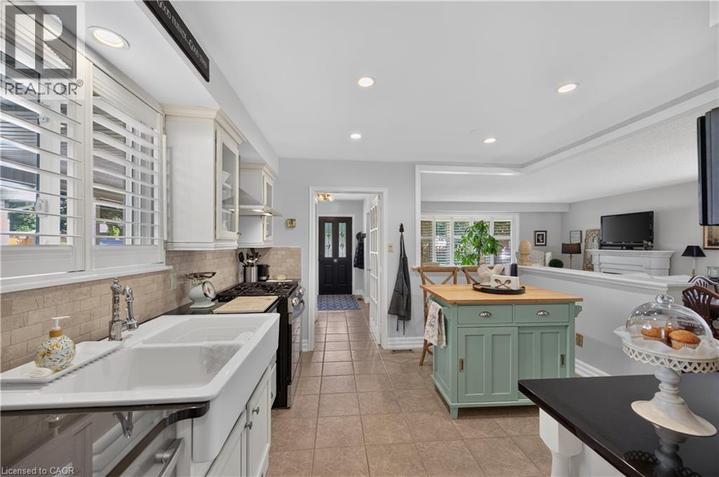 White cabinetry with glass-front accents, farmhouse-style double basin sink, black countertop, recessed lighting, and tile flooring - 1434 Dewbourne Crescent, Burlington, ON