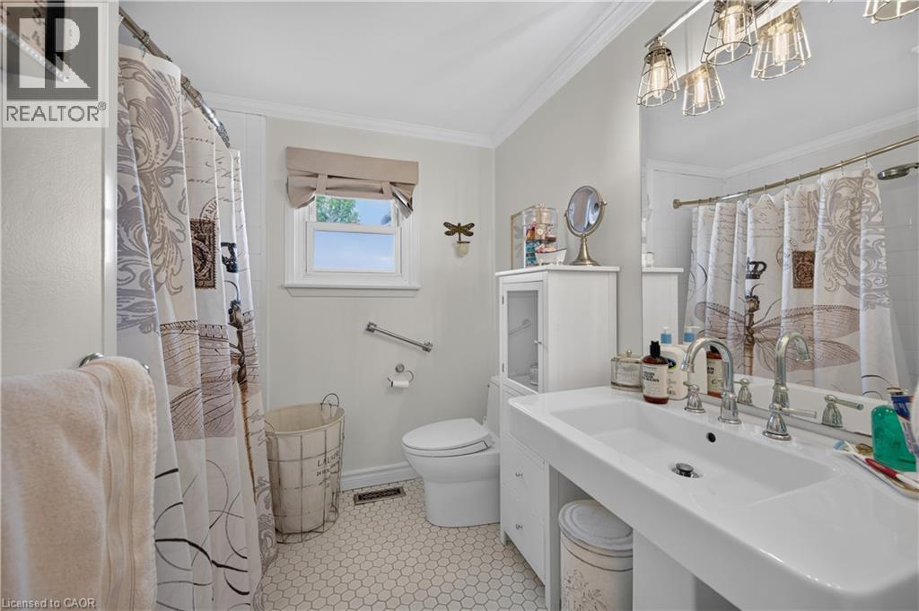 White hex tile flooring, pedestal sink, chrome fixtures, built-in storage cabinet, and window with light-filtering shade - 1434 Dewbourne Crescent, Burlington, ON