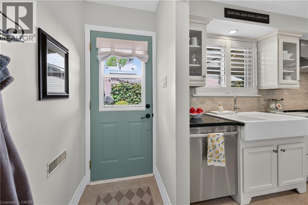Kitchen featuring white cabinetry, a double basin farmhouse sink, stainless steel dishwasher, dark countertop, and tiled backsplash - 1434 Dewbourne Crescent, Burlington, ON