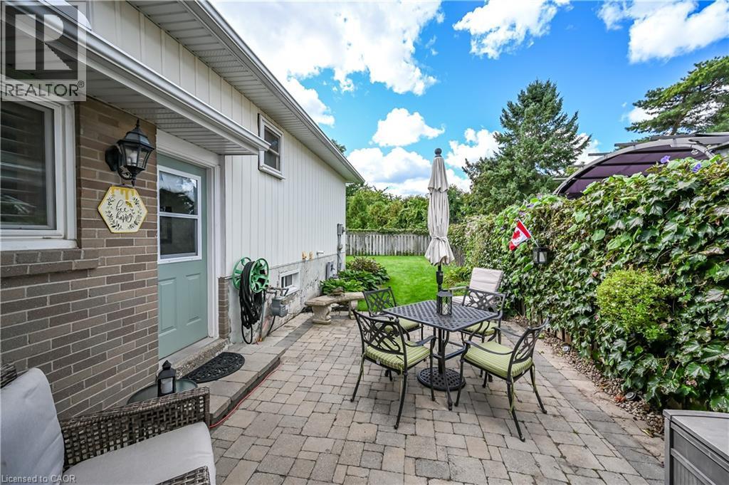 Brick and siding exterior with an accessible side entrance, paver patio, and a privacy fence with established greenery - 1434 Dewbourne Crescent, Burlington, ON