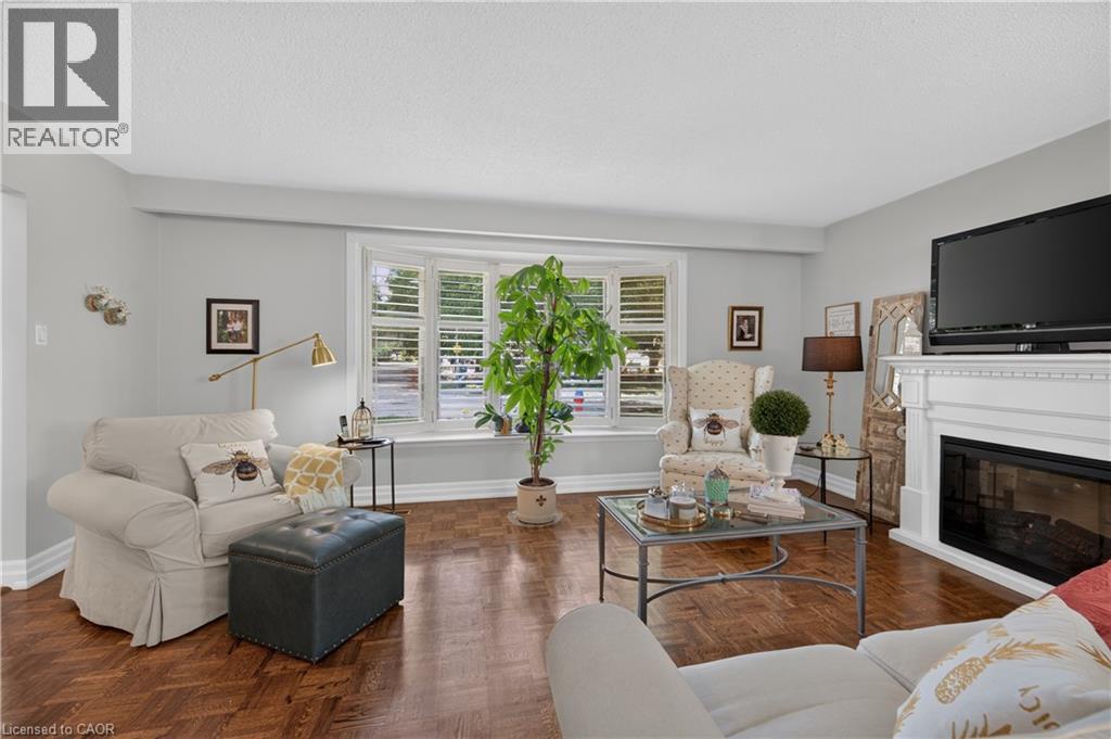 Bay window with white plantation shutters, rich wood-finish flooring, and a white fireplace with a mantel - 1434 Dewbourne Crescent, Burlington, ON