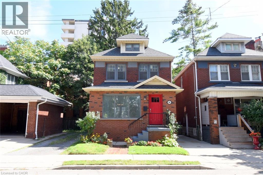 Brick exterior with a prominent red entry door, dormer window, and an attached single-car garage - 35 Tisdale Street S, Hamilton, ON