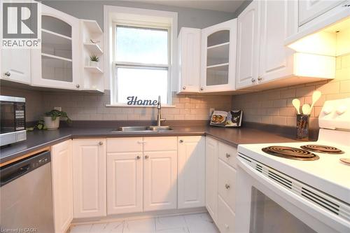 White cabinetry with brushed nickel hardware, solid surface countertops, subway tile backsplash, and a stainless steel sink with a gooseneck faucet - 35 Tisdale Street S, Hamilton, ON 