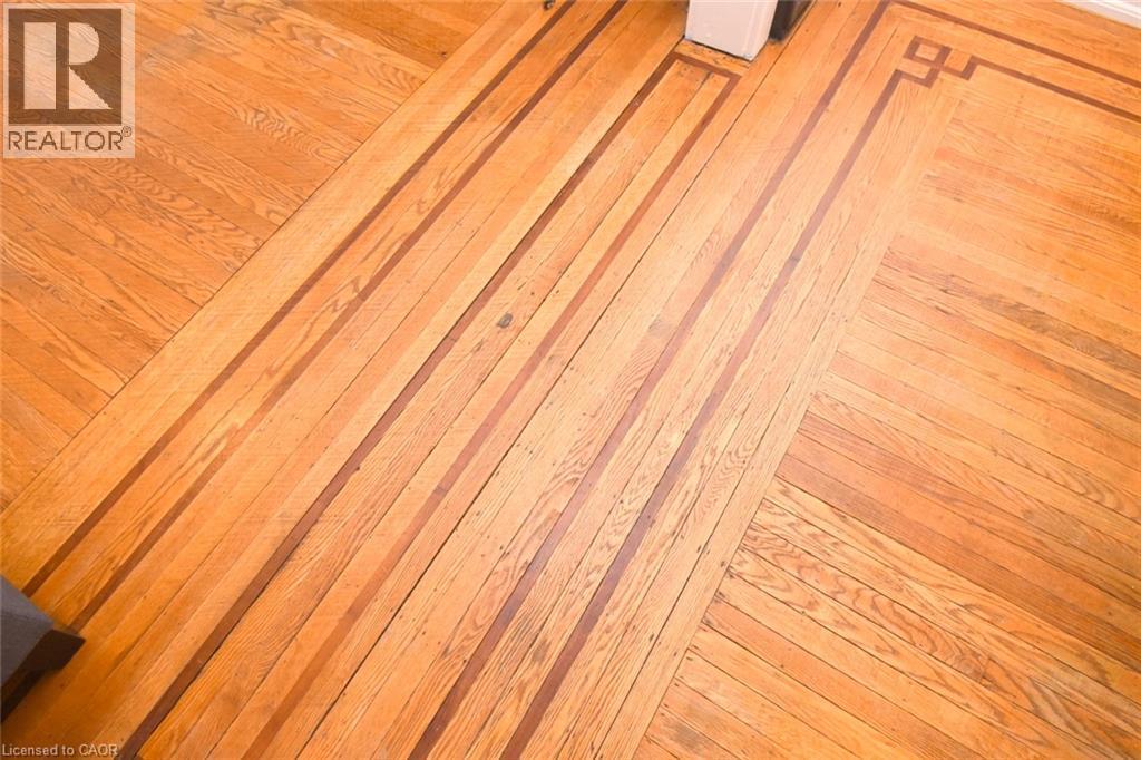 Hardwood flooring throughout featuring warm wood-finish planks laid in a diagonal herringbone pattern, showcasing rich amber and honey tones with natural grain variation and a polished finish - 35 Tisdale Street S, Hamilton, ON