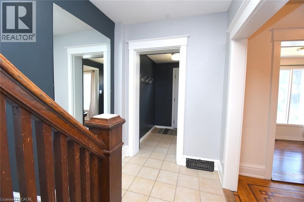 Hardwood staircase with detailed newel post, tiled entry flooring, white trim work, and dark accent wall - 35 Tisdale Street S, Hamilton, ON
