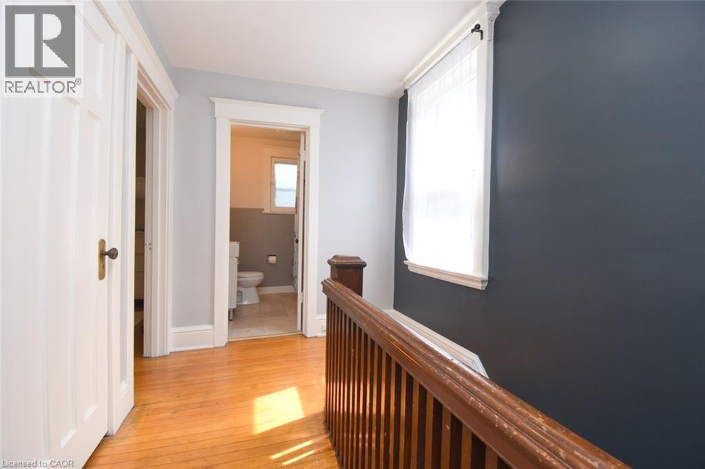 Hardwood flooring, painted interior walls, white trim, wood-finish railing, and a window with sheer curtains - 35 Tisdale Street S, Hamilton, ON