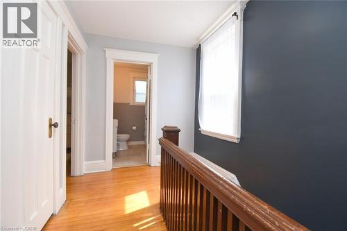 Hardwood flooring, painted interior walls, white trim, wood-finish railing, and a window with sheer curtains - 35 Tisdale Street S, Hamilton, ON 