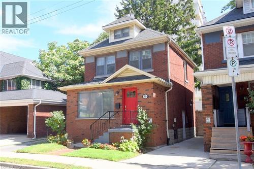 Brick exterior with a prominent red door, front porch with black railings, and a dormer window - 35 Tisdale Street S, Hamilton, ON 