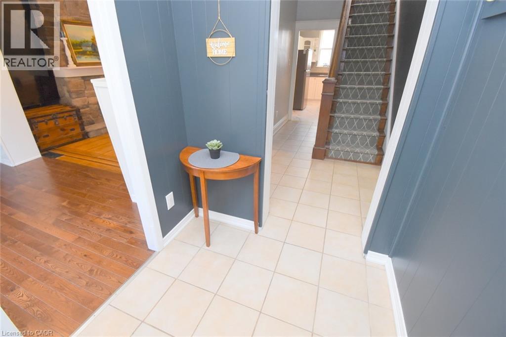 Tiled flooring entry with a wood-finish staircase featuring a patterned runner and dark wood newel post - 35 Tisdale Street S, Hamilton, ON
