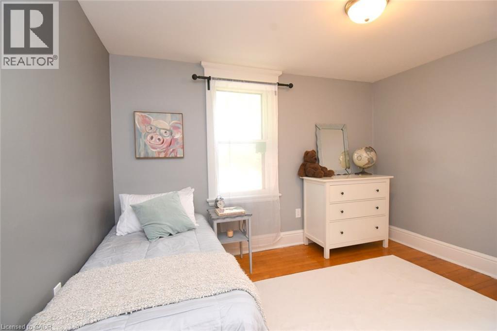 Hardwood flooring, light gray wall paint, window with white trim, and a semi-flush mount ceiling light - 35 Tisdale Street S, Hamilton, ON