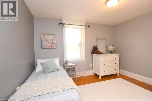 Hardwood flooring, light gray wall paint, window with white trim, and a semi-flush mount ceiling light - 35 Tisdale Street S, Hamilton, ON 