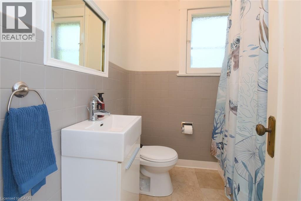 Compact bathroom featuring a window, tile flooring, wall-mounted vanity with a rectangular basin, and a mirrored medicine cabinet - 35 Tisdale Street S, Hamilton, ON