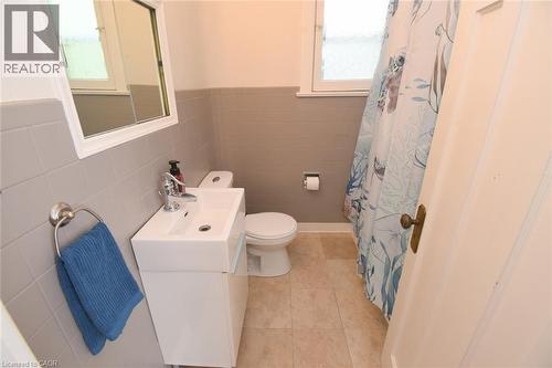 White vanity with integrated sink, chrome faucet, tiled flooring, and tiled wall surround - 35 Tisdale Street S, Hamilton, ON 
